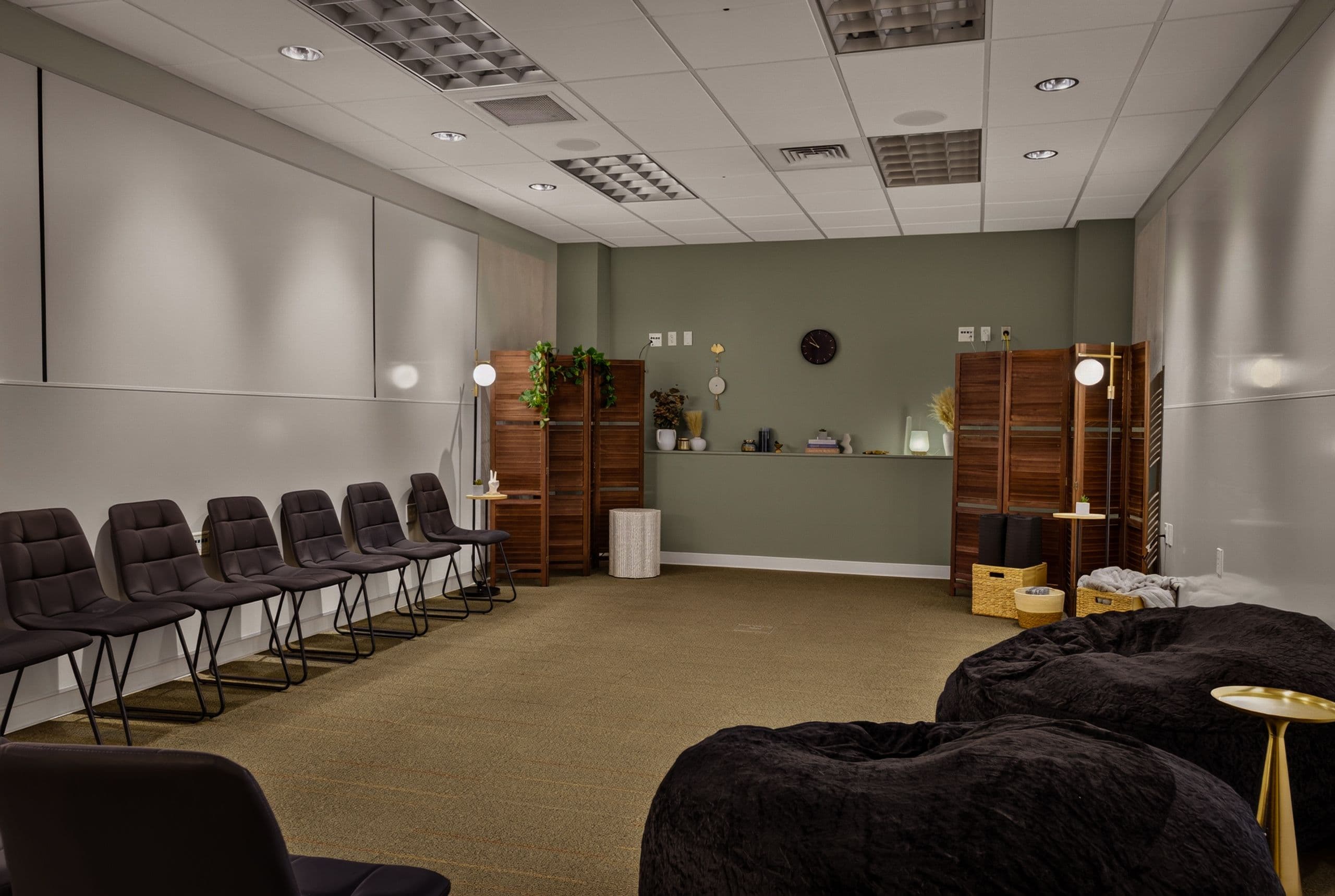 A calm, dimly lit room with bean bags, chairs and wooden screens